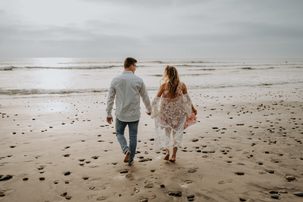 Couple on beach holding hands walking on sand | Southern California Wedding Photographer