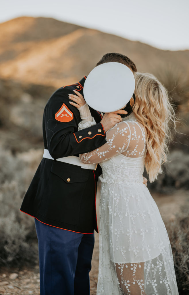 couple kissing behind hat during engagement photoshoot in Joshua Tree