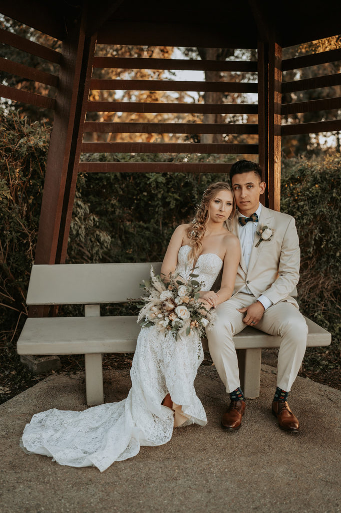bride and groom sitting on bench at park for wedding photo session