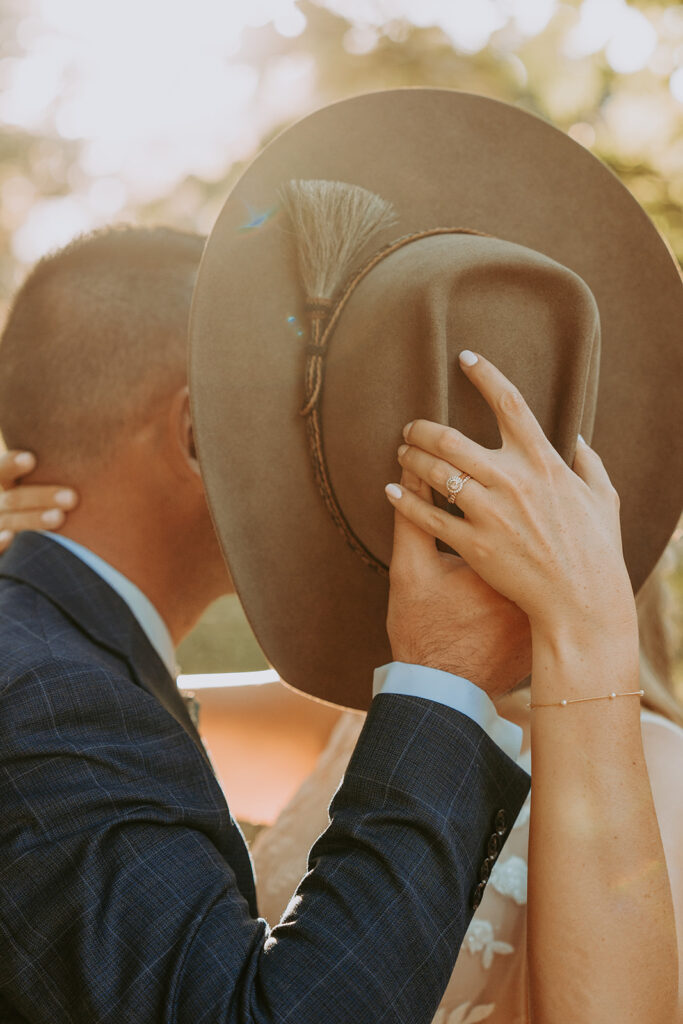 bride and groom kissing behind a cowboy hat