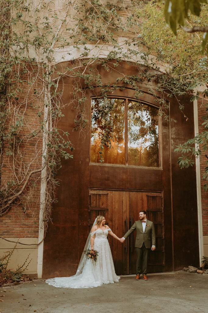 bride and groom standing against a large brick building