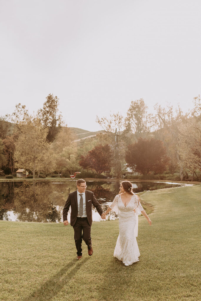 bride and groom running toward the camera in front of a lake