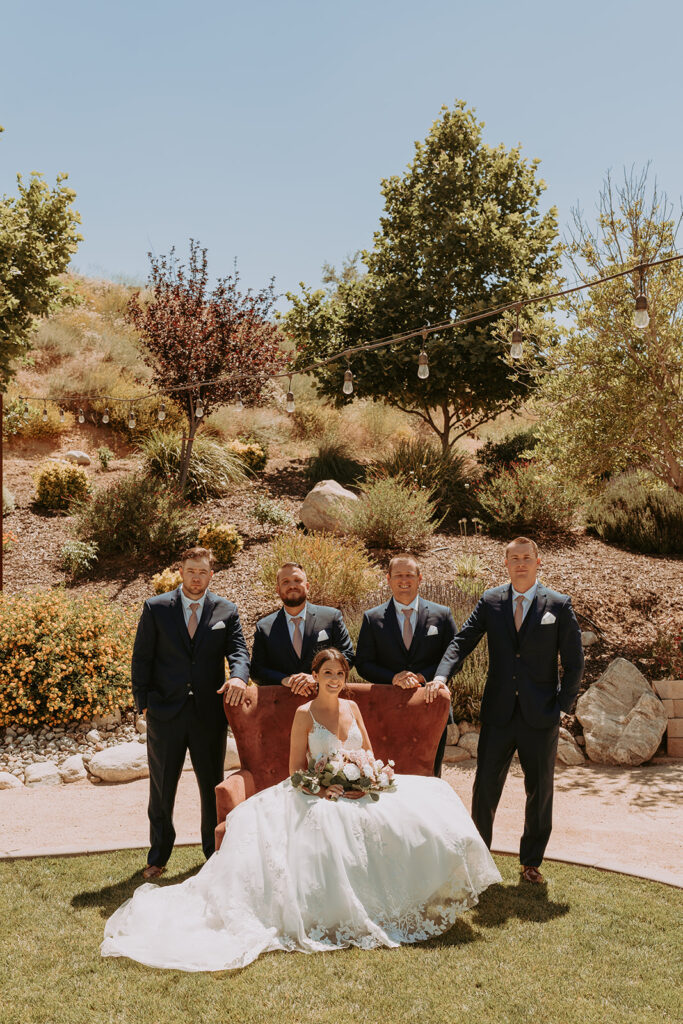 bride sitting in a large chair with groomsmen behind her