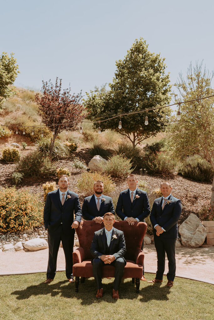 groom sitting in a large chair with his groomsmen behind him