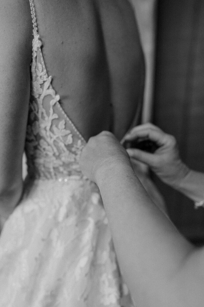 bride getting ready and buttoning her dress