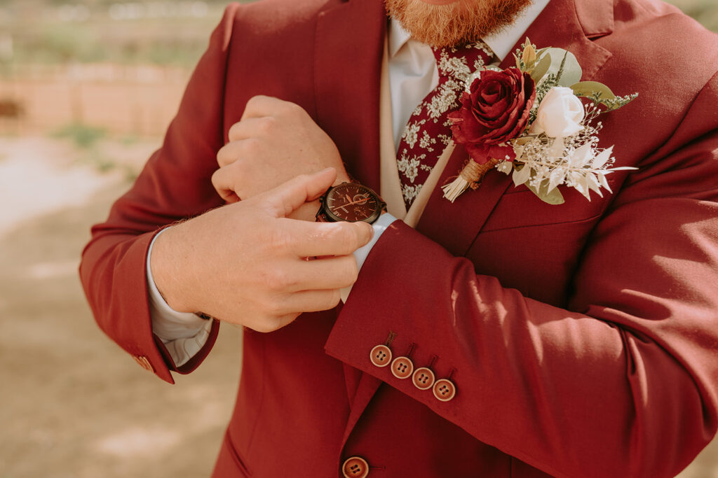 close up of a groom in a red suit with a watch