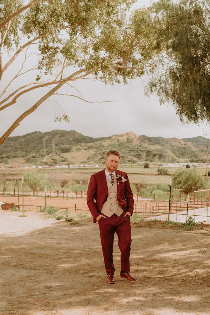 groom posing at a ranch in a red suit
