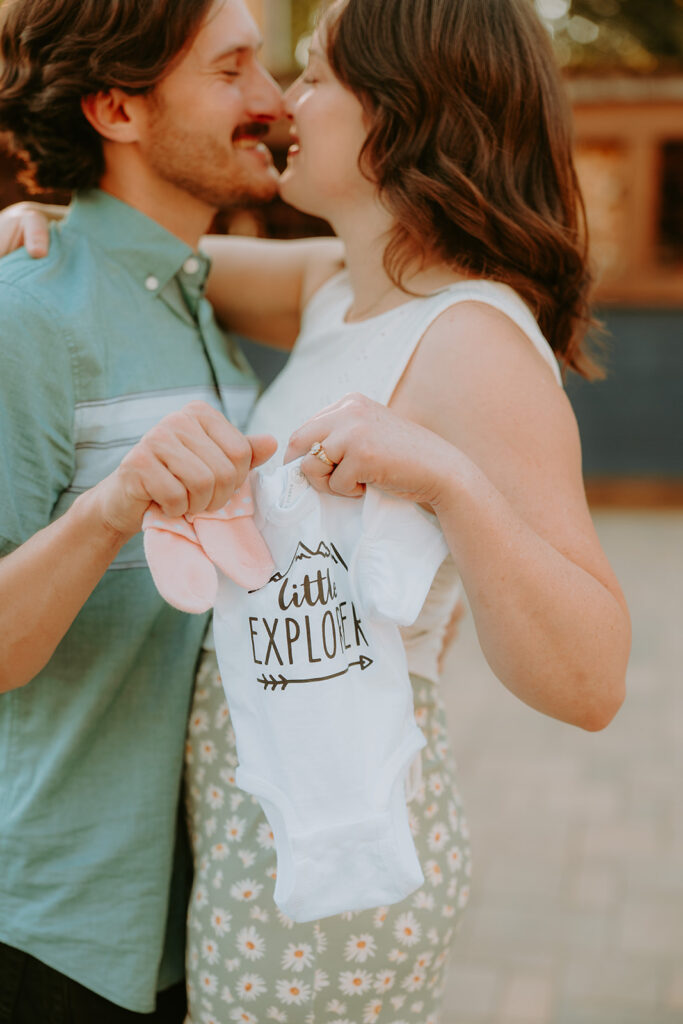couple holding a newborn onesie for a baby announcement